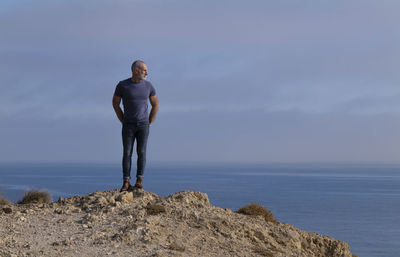 Full length of adult man in jeans on seaside against sky. cabo de gata nature park, almeria, spain