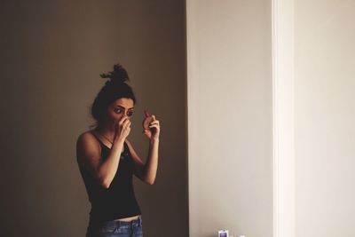 Woman applying mascara while standing at home