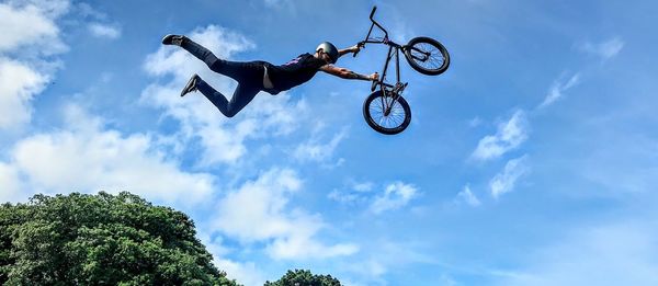 Low angle view of boy jumping with bicycle while doing stunt against sky