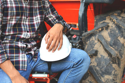 Midsection of worker holding hardhat while sitting outdoors