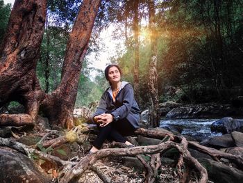 Portrait of young woman sitting on tree trunk in forest