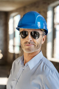 Architect wearing sunglasses and hardhat smiling while standing at construction site