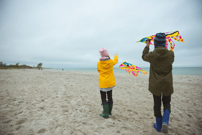 Rear view of boy holding kite standing on beach against sky