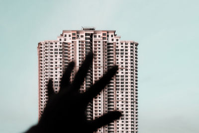 Cropped hand gesturing towards modern building against clear sky