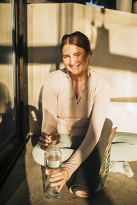 Portrait of happy woman opening water bottle while sitting cross-legged at retreat center