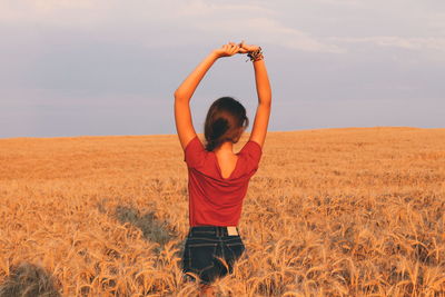 Rear view of young woman with arms raised standing on field