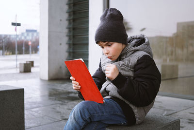 Boy using digital tablet while sitting on seat during winter