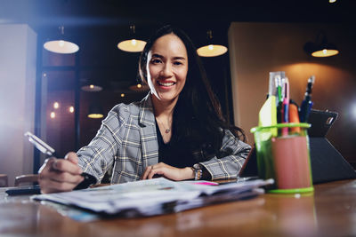 Portrait of smiling businesswoman writing on document while sitting in office