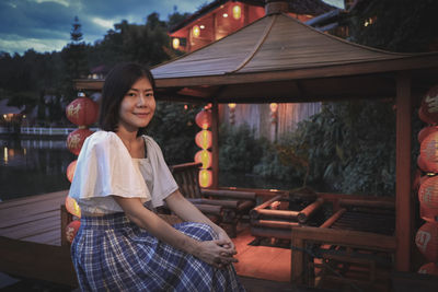 Portrait of woman sitting by gazebo at dusk