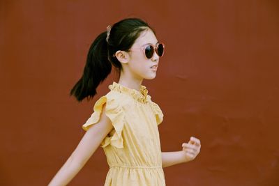 Girl wearing sunglasses looking away while standing against wall