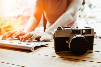 Midsection of woman typing on keyboard by camera at table