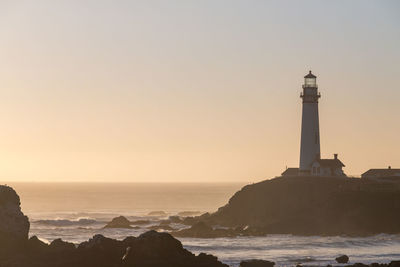 Lighthouse by sea against sky during sunset