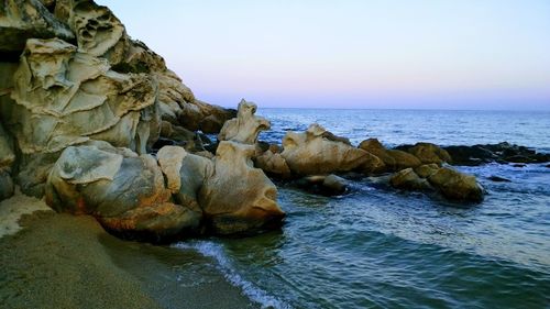 Rock formation in sea against clear sky