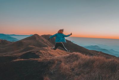 Rear view of man jumping on mountain against clear sky during sunset