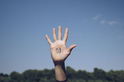 Cropped hand of person with numbers on palm against sky