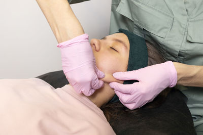 Beautician doing facial massage, beauty procedure to caucasian young teenage girl in spa salon