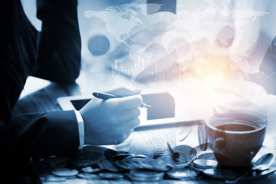 Midsection of man with pen by coins and coffee against world map