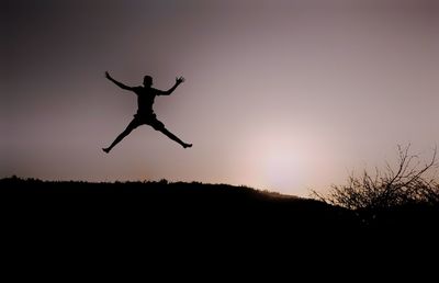 Silhouette man jumping on field against clear sky at sunset