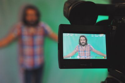 Man standing against green wall displayed on camera