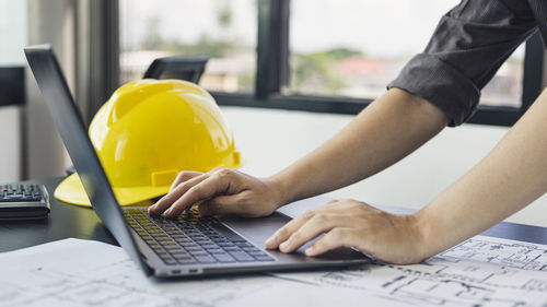 Young man with a laptop plotting a system of building structures in blueprints