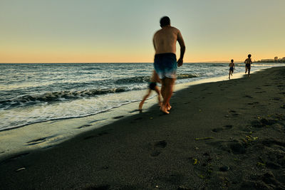 Full length of shirtless man on beach against sky during sunset