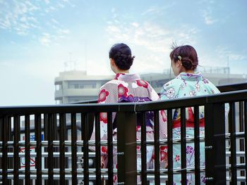 Rear view of woman wearing kimono walking by railing against sky