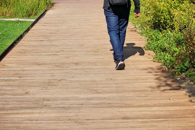 Low section of man walking on boardwalk during sunny day