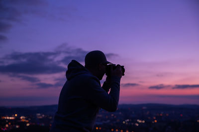 Side view of man photographing against sky during sunset