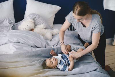 Mother dressing baby boy on bed at home