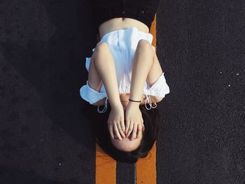 Directly above shot of woman covering face while lying on road