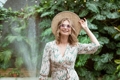 Beautiful young woman in a straw hat and glasses in the park on a background of greenery