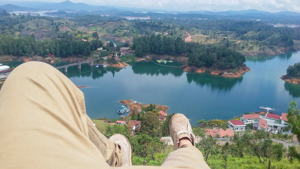 water, lake, building exterior, tree, river, built structure, architecture, person, sky, leisure activity, lifestyles, personal perspective, men, low section, mountain, nature, high angle view, outdoors