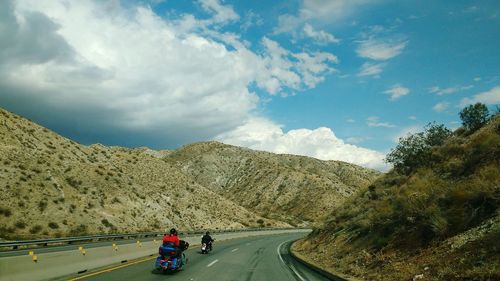 Rear view of people riding motorcycles by mountain on road