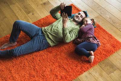 Father and daughter lying on carpet on the floor using digital tablet