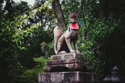 Statue of dog by plants against trees
