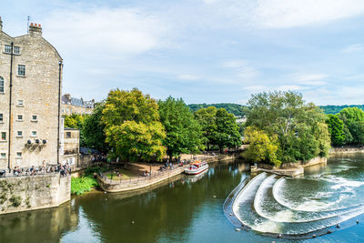 Arch bridge over river amidst trees and buildings against sky