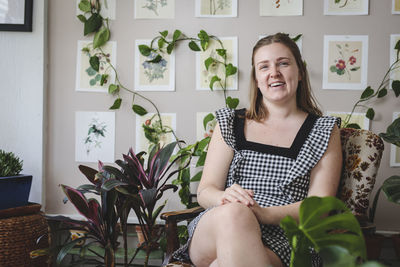 Stylish young woman smiles while sitting in chair with plants