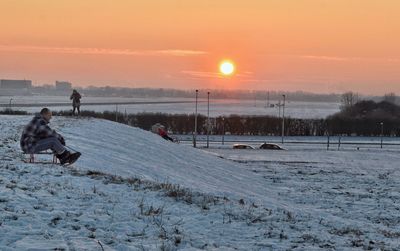 Man standing on snow covered landscape against sky during sunset