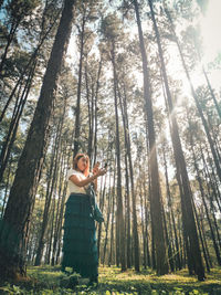 Woman standing by tree trunk in forest