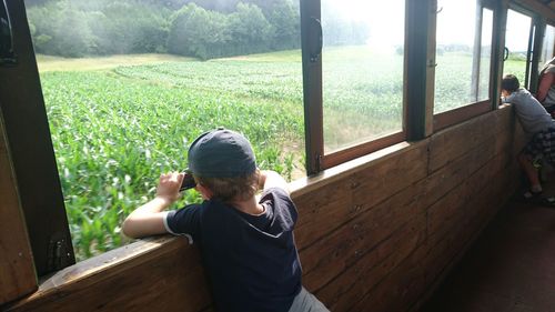 Rear view of boys leaning on window against field