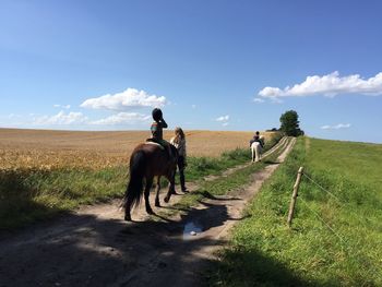 Mother with sons riding horses on pathway amidst grassy field against sky