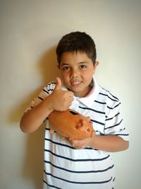 Portrait of boy with piggy bank showing thumbs up at home