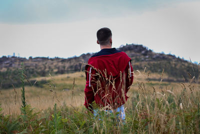 Rear view of man standing on grassy field against sky