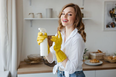 Beautiful girl in yellow gloves holding a cleaning spray in the kitchen