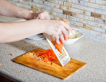 Cropped hands grating carrot in kitchen at home