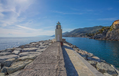 Lighthouse amidst sea and buildings against sky