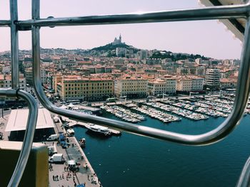 Boats moored at harbor in city seen through railing of ferris wheel