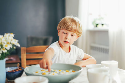 Cute boy playing with flowers kept in bowl while sitting on dining table at home