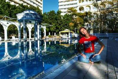 Full length of woman with eyes closed sitting at poolside