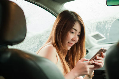 Portrait of young woman using mobile phone in car